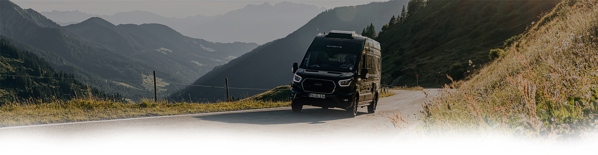 Ein schwarzes Allrad-Wohnmobil auf einer Straße in einer Berglandschaft.