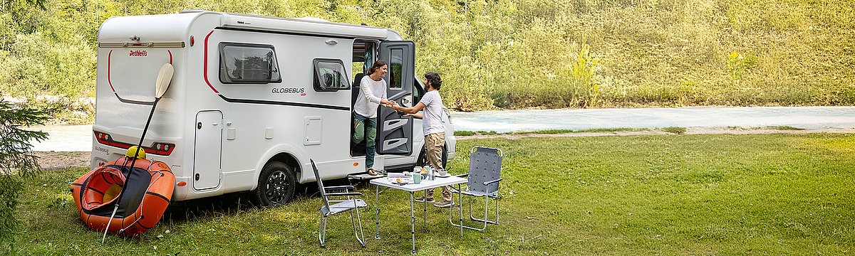 Ein Wohnmobil der Marke Dethleffs auf einer Wiese an einem Gewässer.