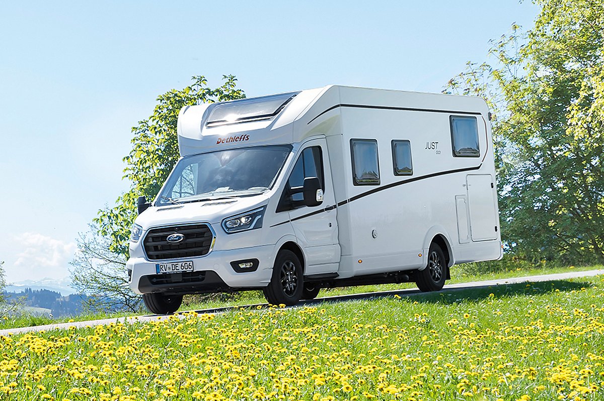 Ein weißes Wohnmobil der Marke Dethleffs fährt an einer gelb blühenden Wiese vorbei.