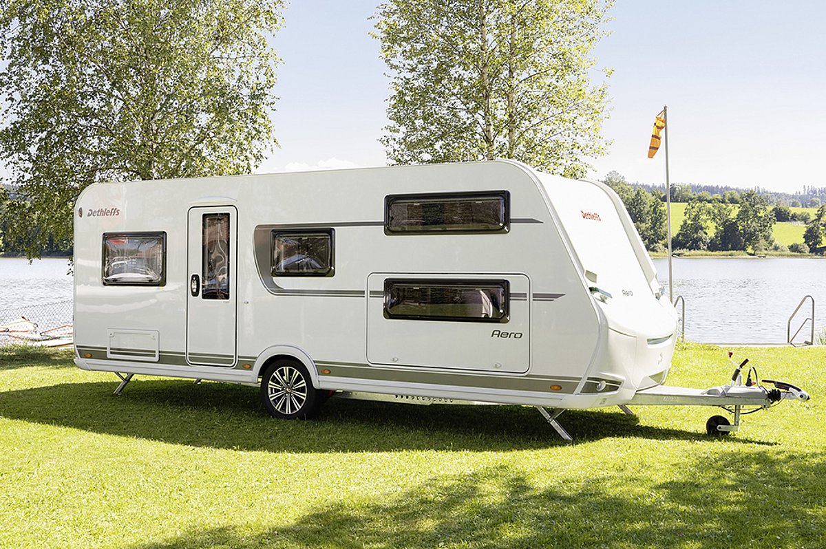 Ein weißer Camper des Herstellers Dethleffs auf einer grünen Wiese vor einem See.