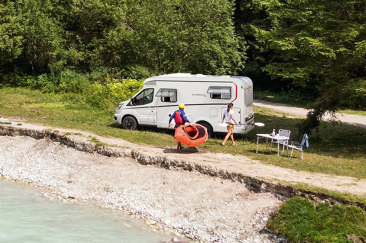 Eine Frau sitzt an einem Tisch vor einem Wohnmobil, ihr gegenüber steht ein Mann.