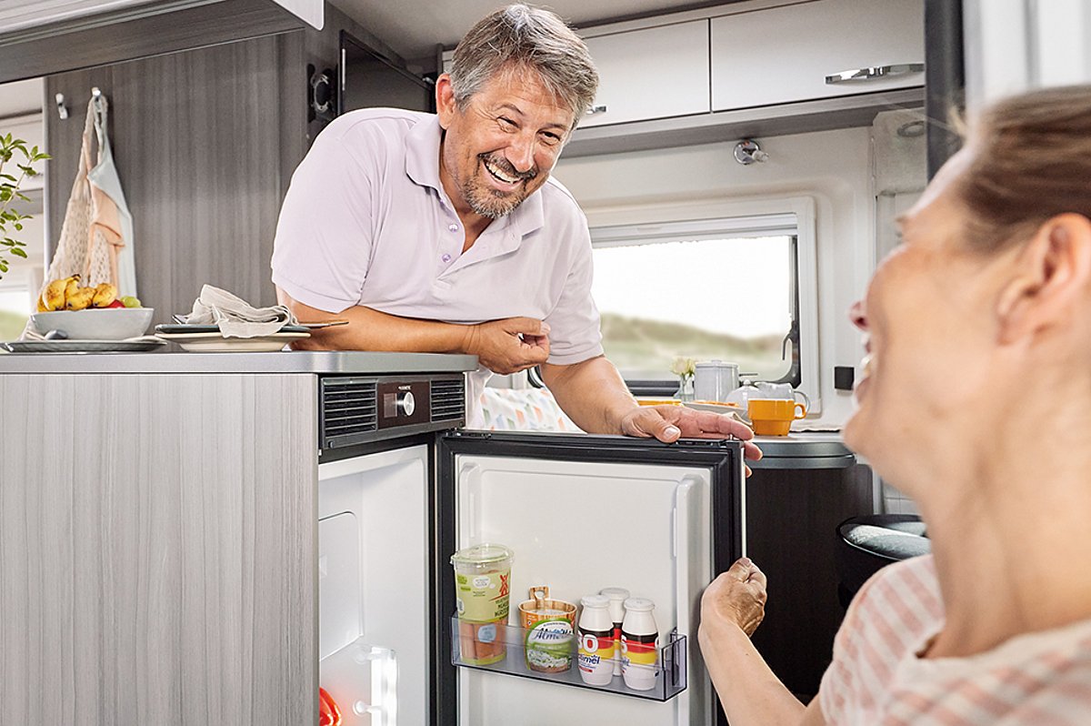 Eine Frau und ein Mann öffnen gemeinsam einen Kühlschrank in einem Wohnmobil.