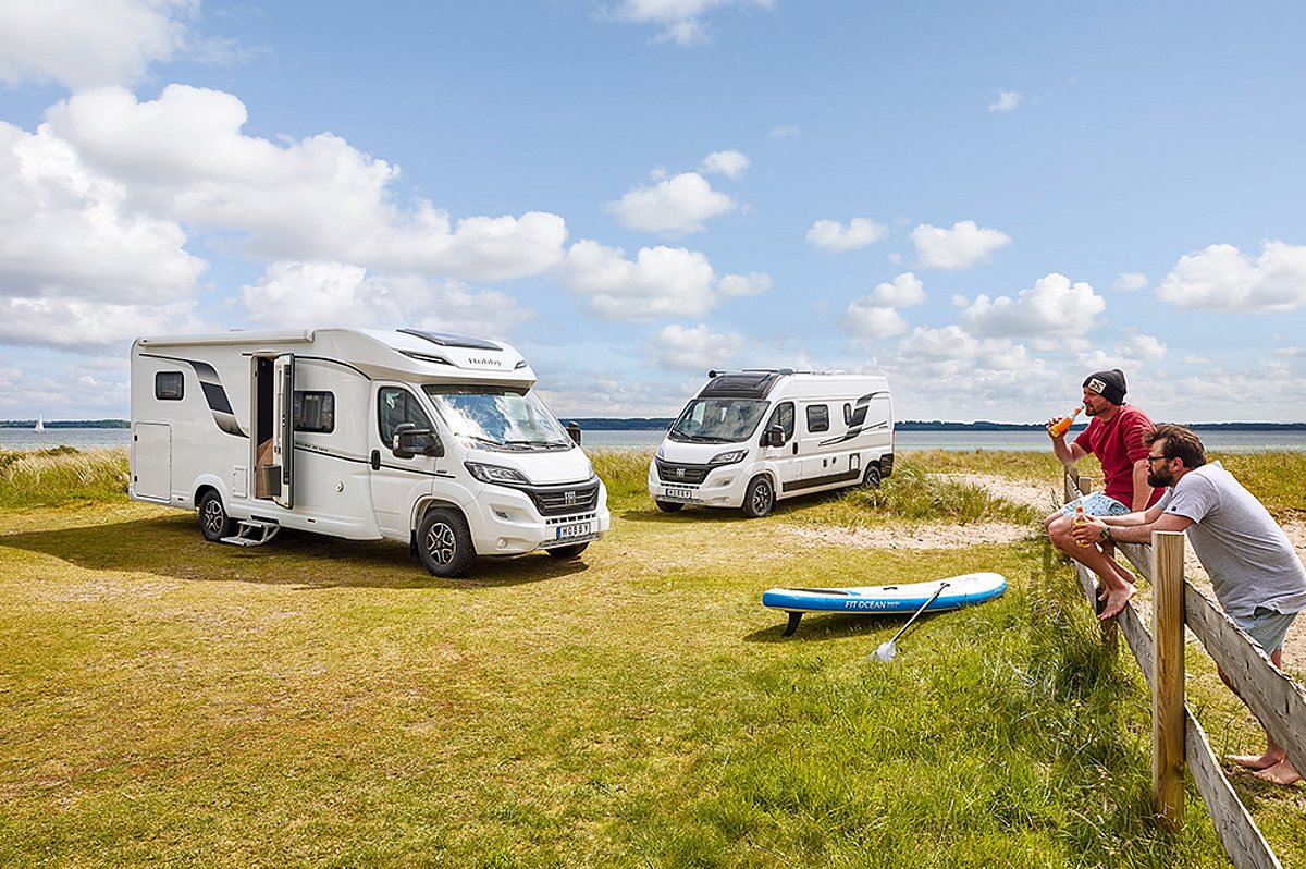 Zwei Wohnmobile auf einer Wiese. Zwei Personen befinden sich am rechten Bildrand.