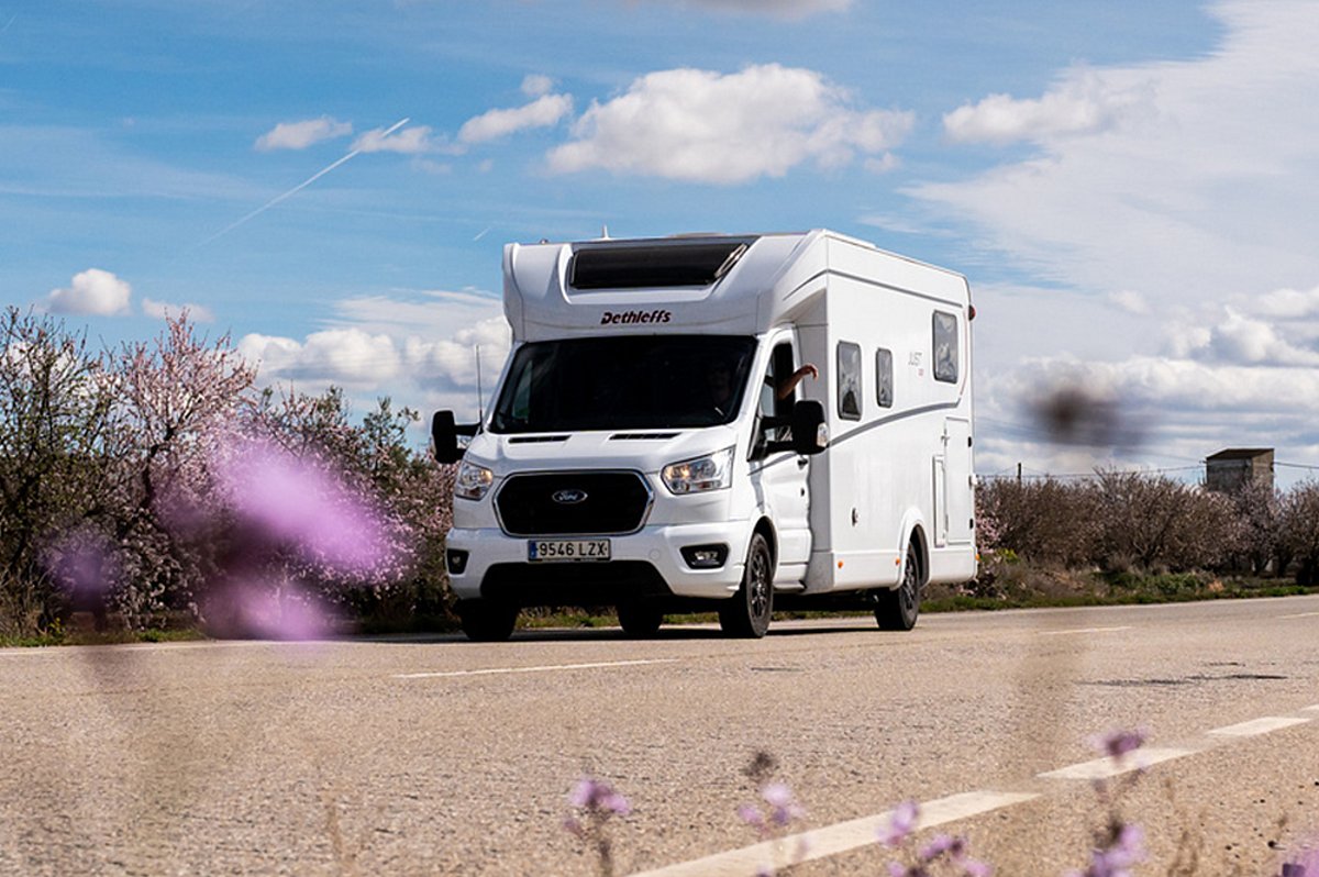 Ein weißes Wohnmobil der Marke Dethleffs auf einer Straße mit blühenden Blumen im Vordergrund.