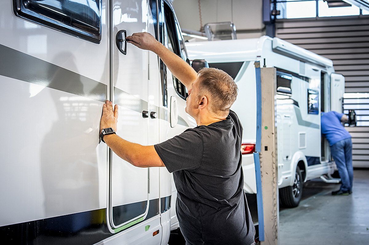 Ein Mitarbeiter von Caravanzeit justiert einen Türgriff an einem Wohnmobil.