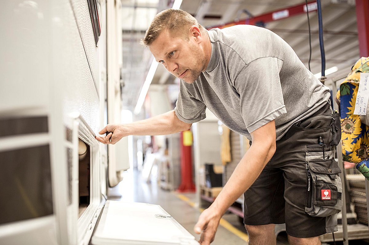 Ein Mitarbeiter von Caravanzeit kontrolliert in der Werkstatt eine Klappe an einem Wohnmobil.